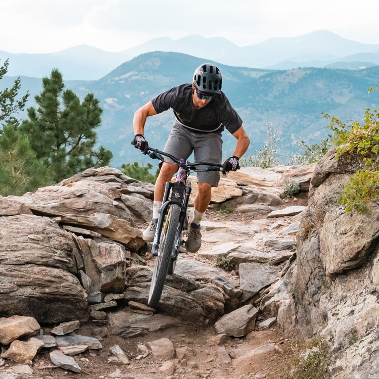 Person mountain biking on a rocky trail with mountains in the background