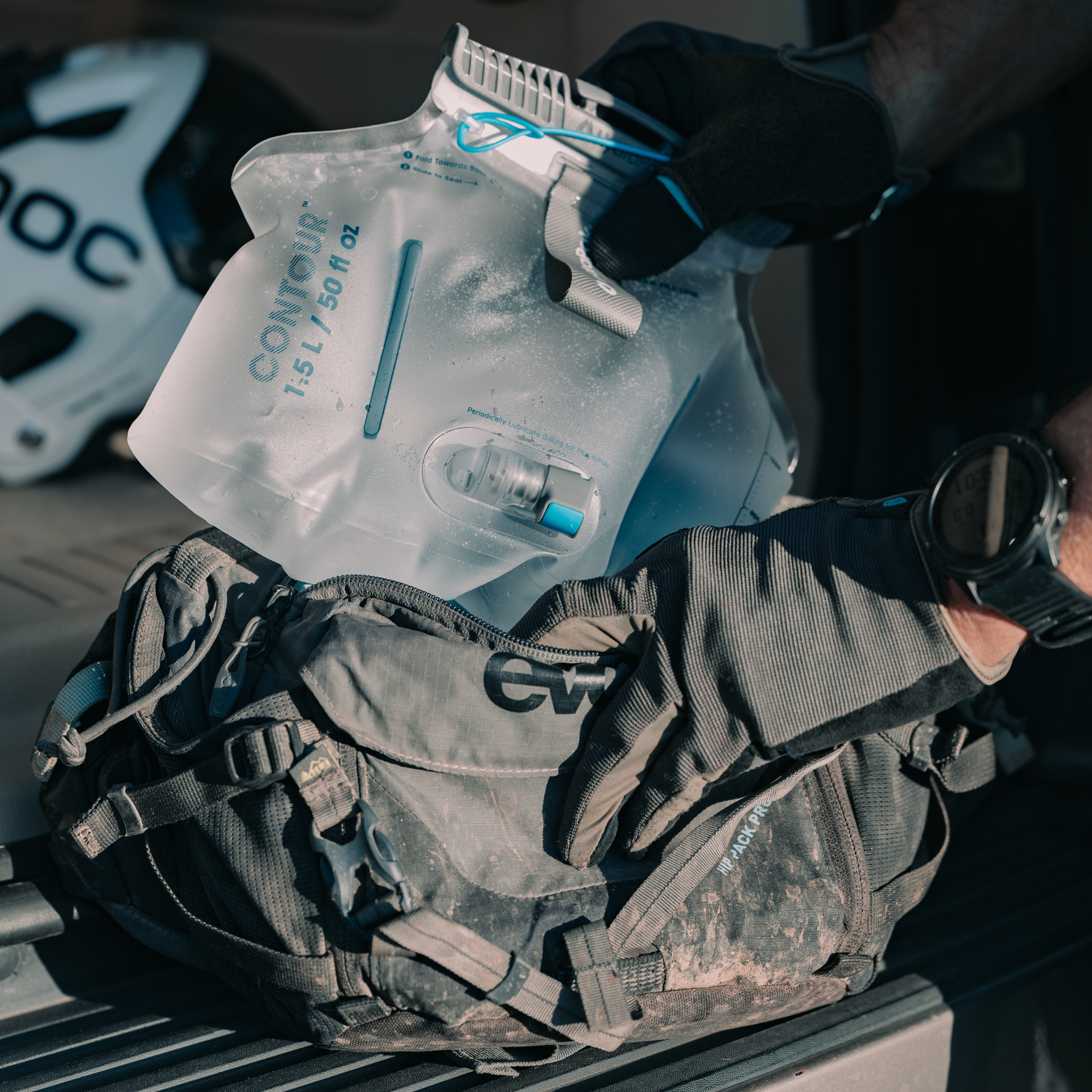Person holding a HydraPak 1.5 litre Contour Hydration Pack with a helmet and backpack in the background
