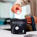 Person holding a gear cleaning tablet above a package of 'Bottle Bright' tablets.